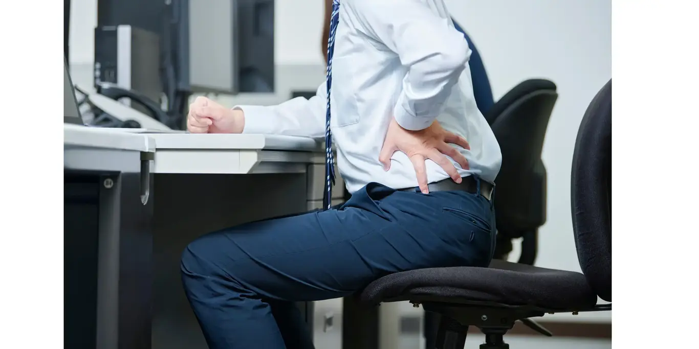 a man holding his back while sitting at a desk