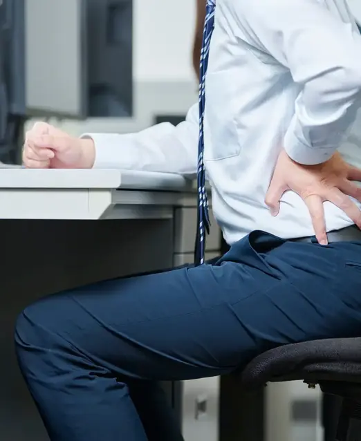 a man holding his back while sitting at a desk