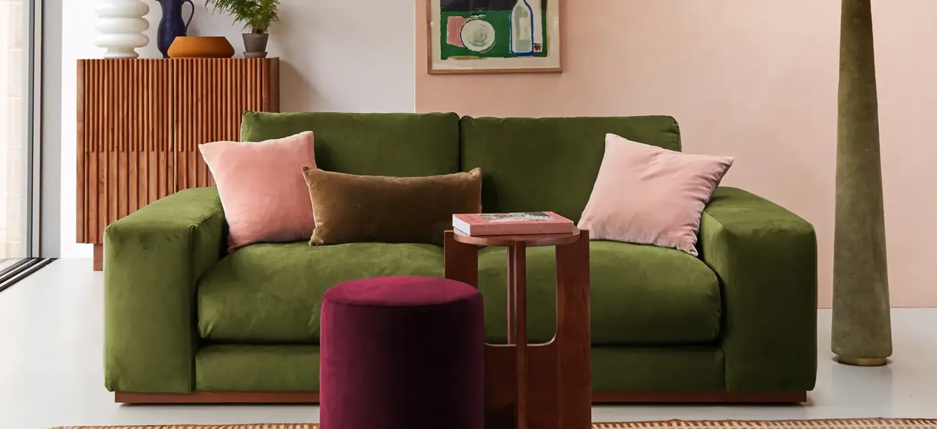 a green couch with pink pillows and a red stool