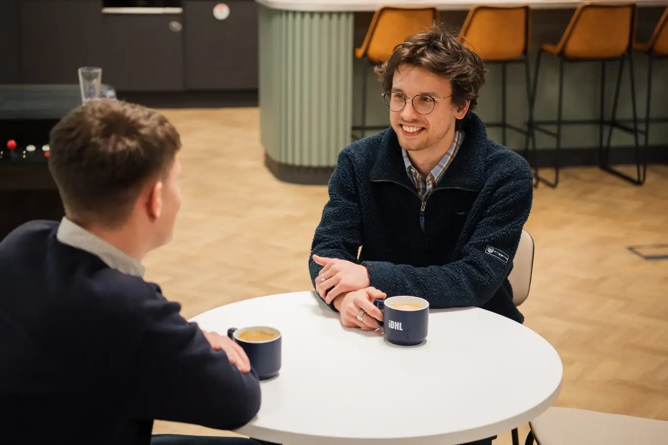 two men sitting at a table with coffee cups