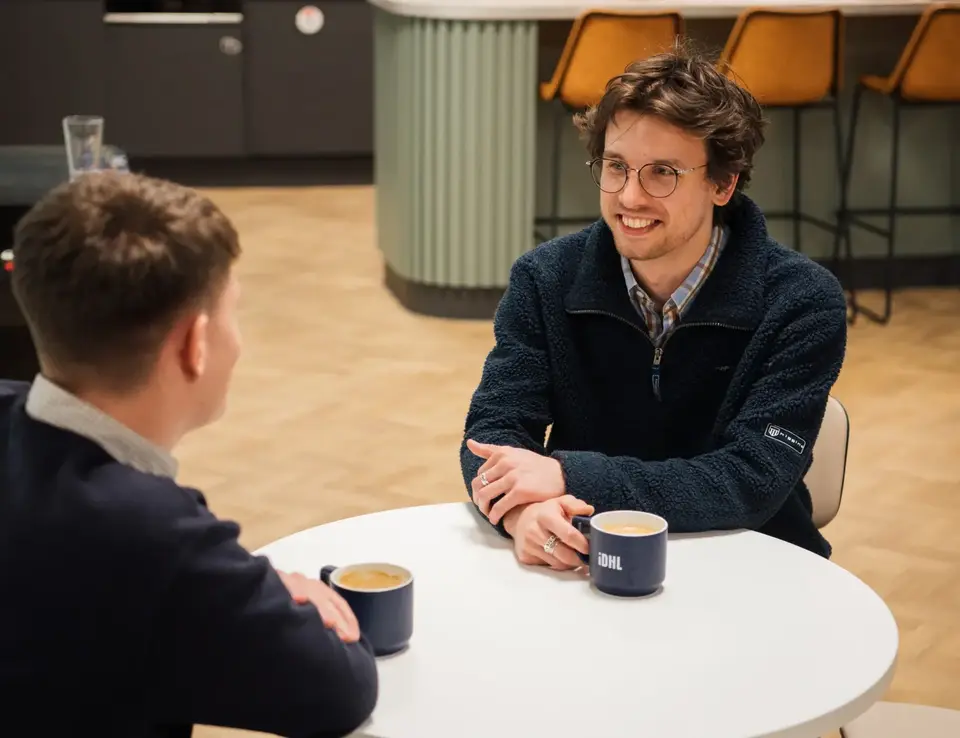 two men sitting at a table with coffee cups