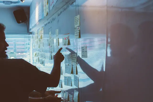 a person pointing at sticky notes on a wall
