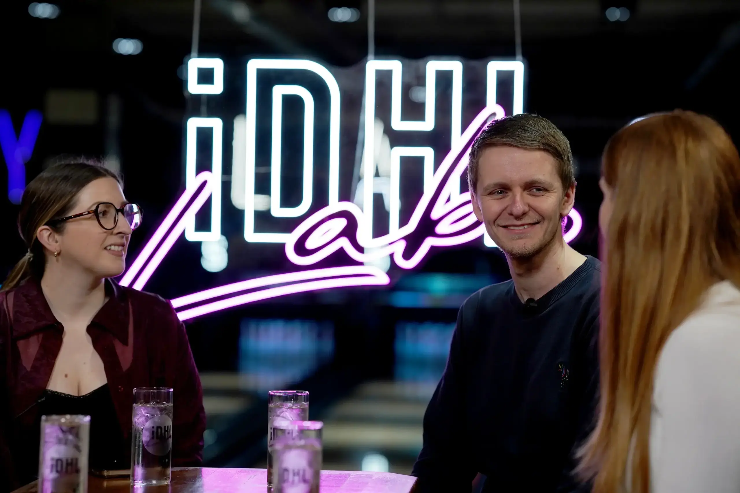 Three people sitting and drinking water with an IDHL Labs neon sign