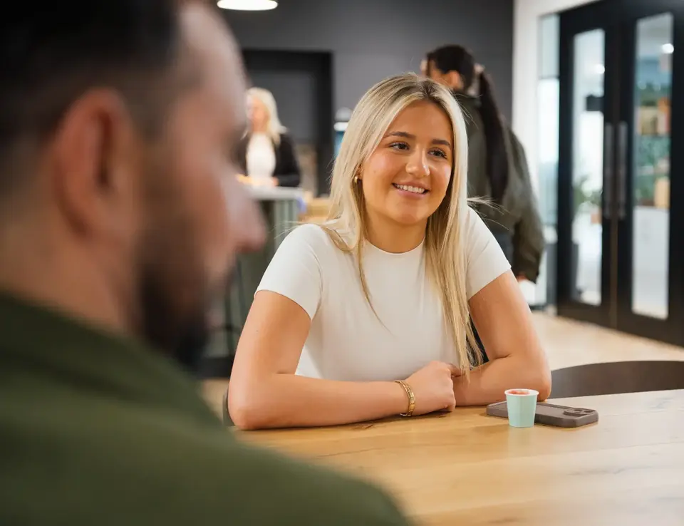 a woman sitting at a table with a man in the background