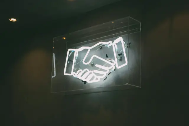 a neon sign with handshake on a wall