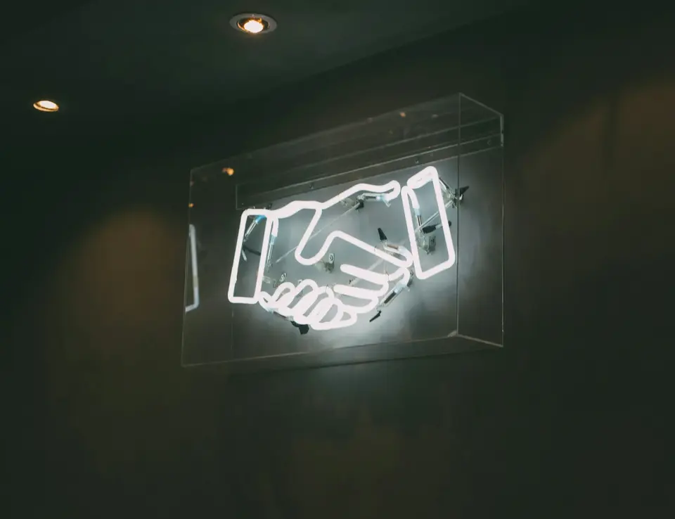 a neon sign with handshake on a wall