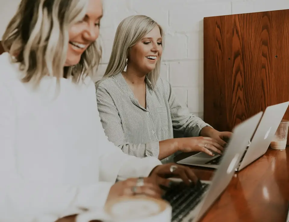 two women sitting at a table with laptops