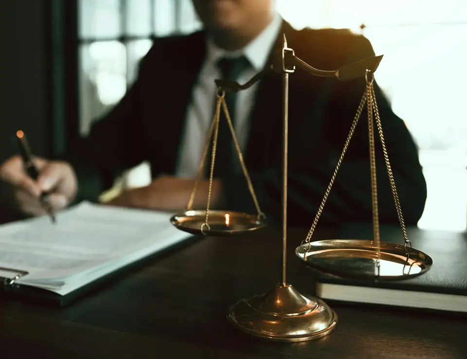 A man in a suit sitting at a table with a gold scale