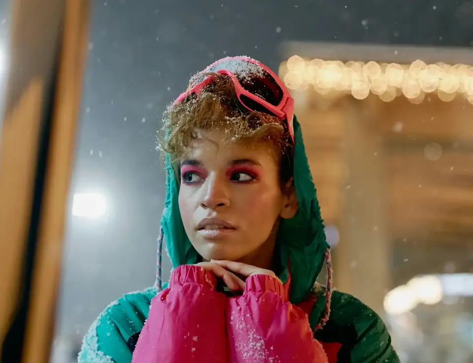 a woman wearing pink and green jacket with pink goggles and pink eye makeup
