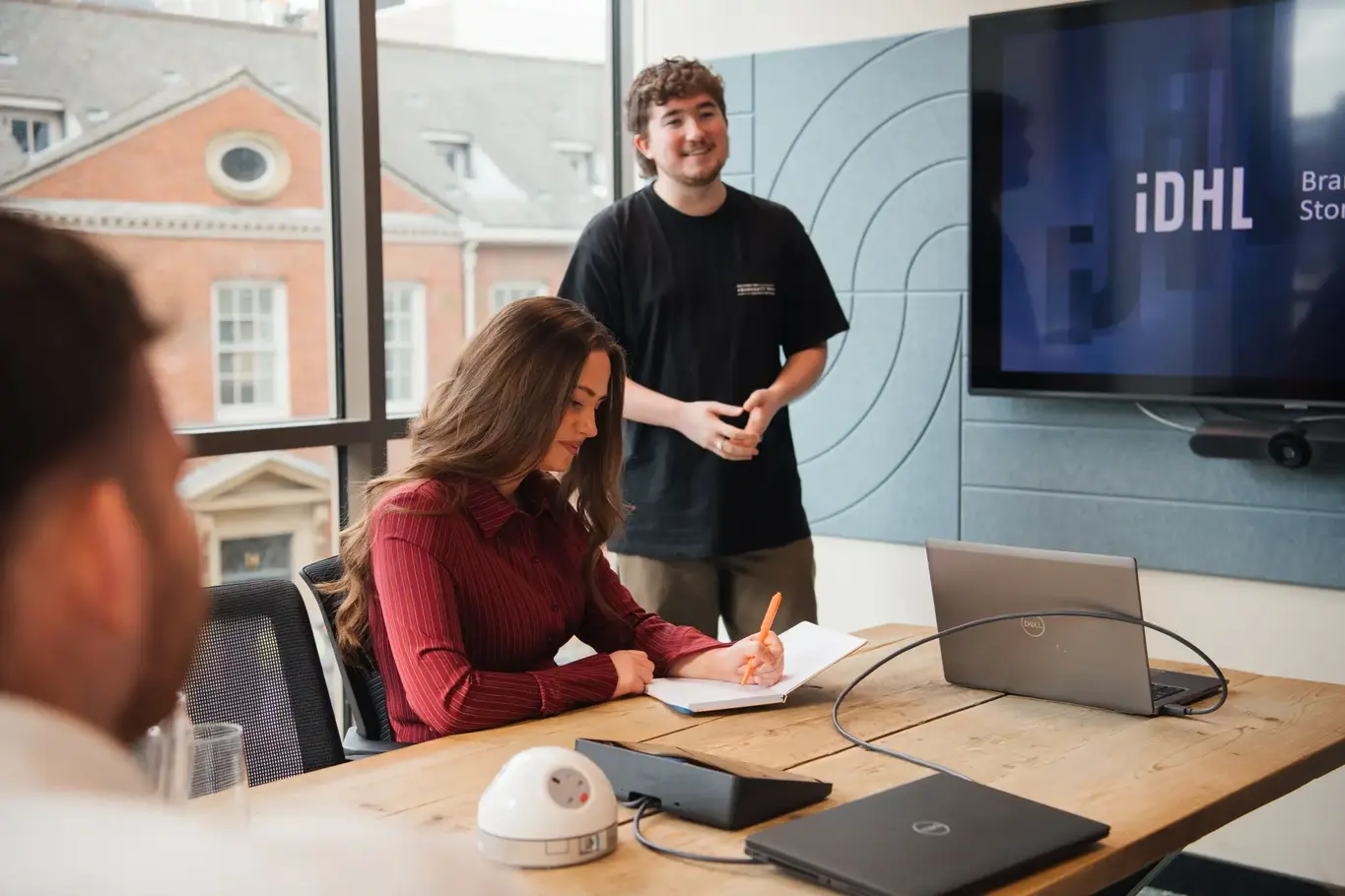 a man standing behind a woman writing on a notebook