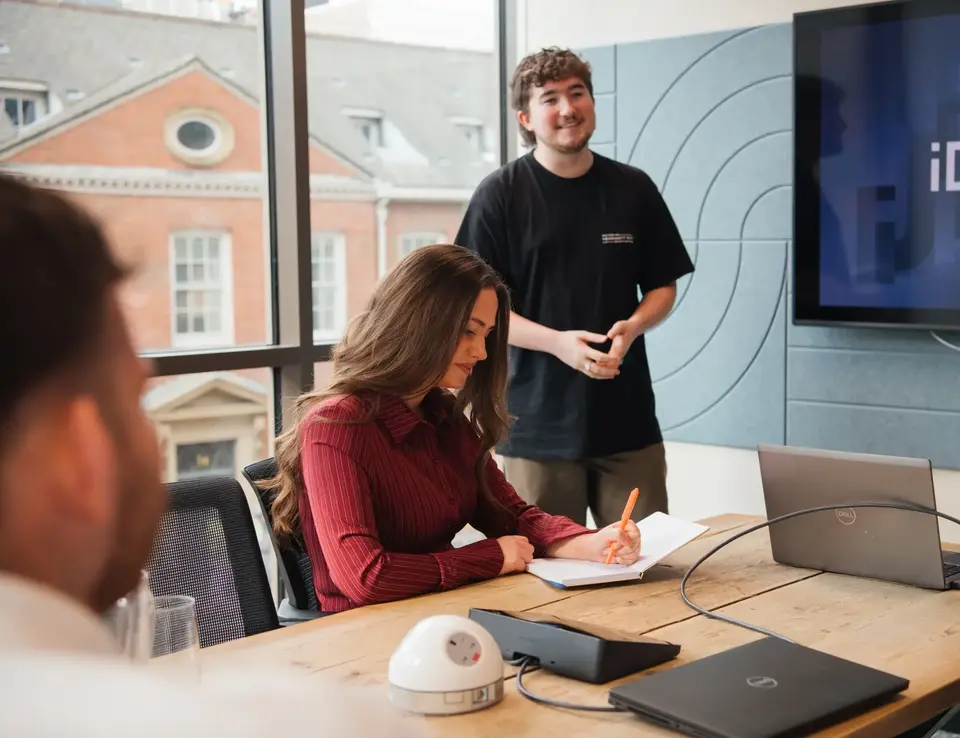 a man standing behind a woman writing on a notebook