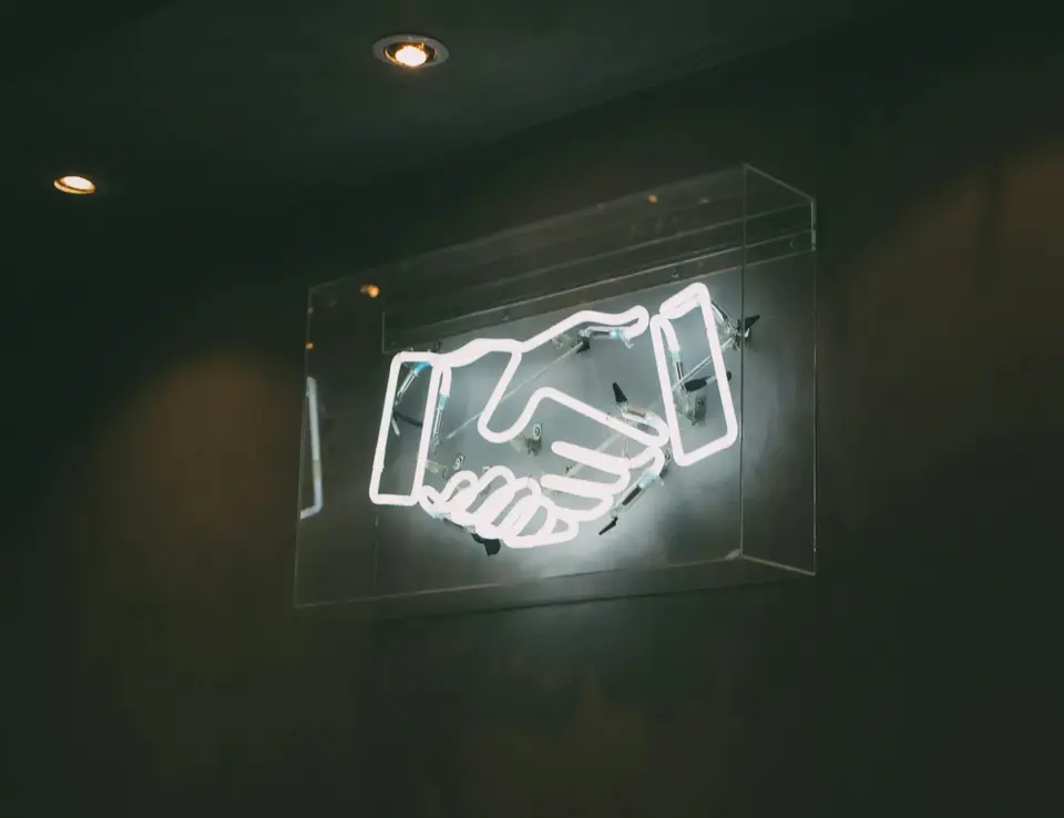 A neon sign of a handshake on a wall