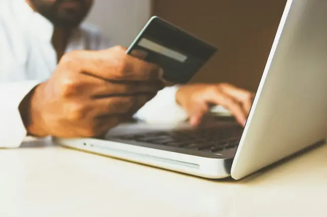 a person holding a credit card and typing on a laptop