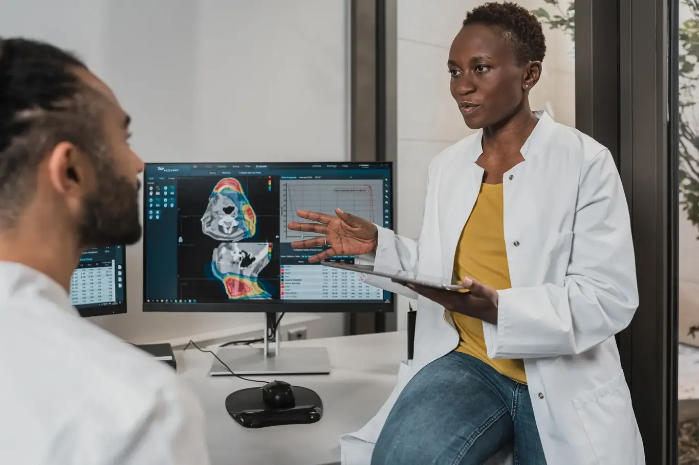 a woman in a white coat talking to a man in front of computer screens