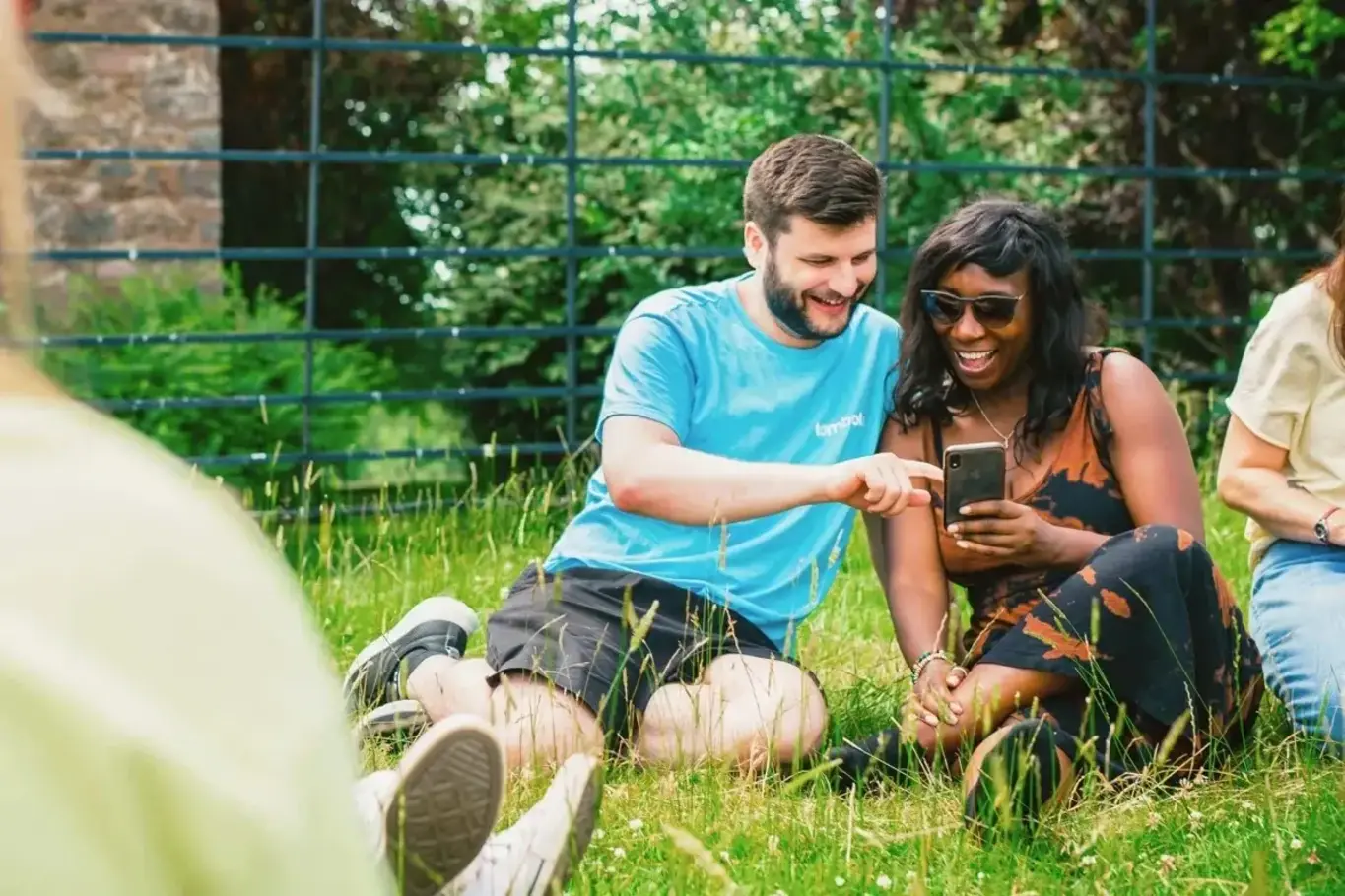 a man and woman sitting on grass looking at a phone
