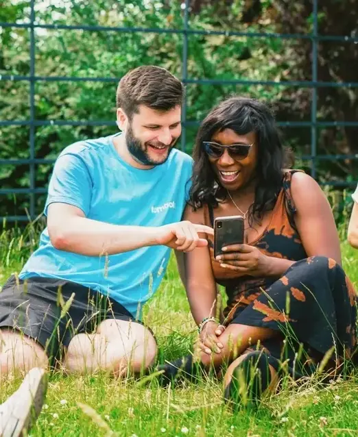 a man and woman sitting on grass looking at a phone