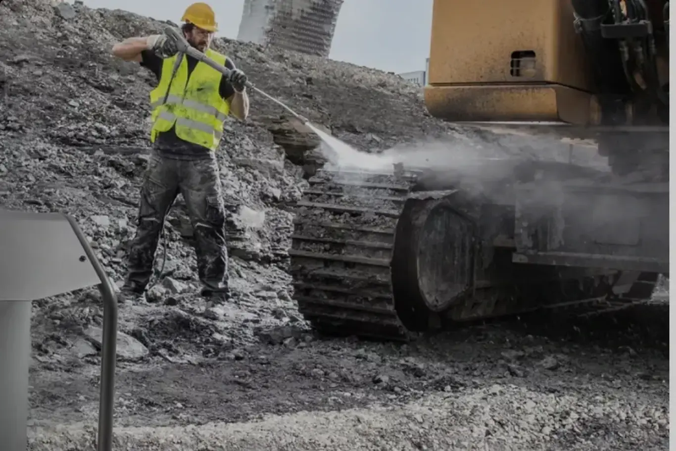 a man in a yellow vest spraying dirt on a large machine