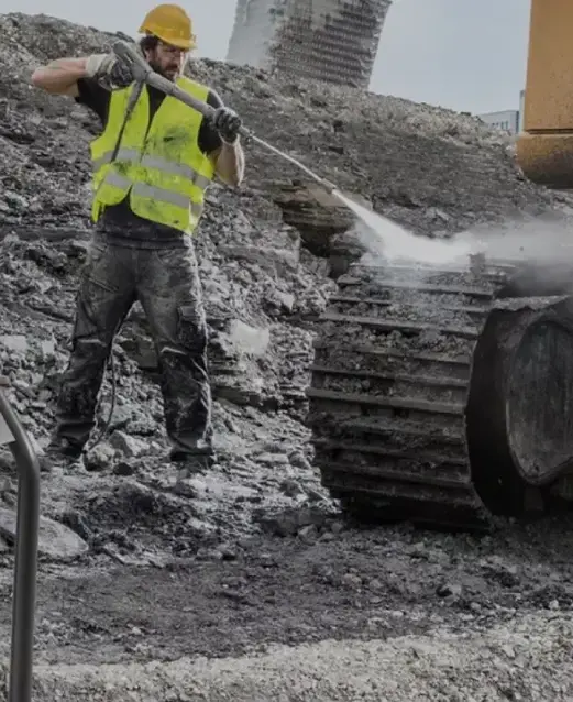 a man in a yellow vest spraying dirt on a large machine
