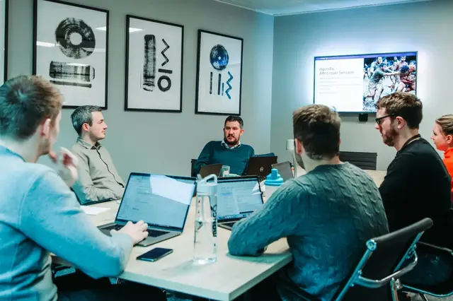 a group of men sitting around a table with laptops