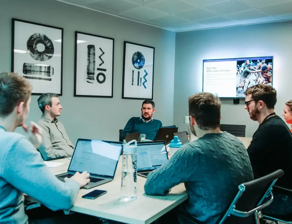a group of men sitting around a table with laptops