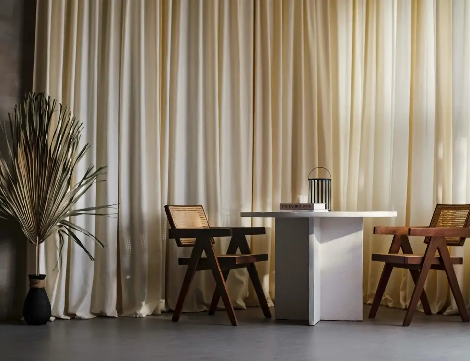 a white table with chairs and a plant in front of a curtain