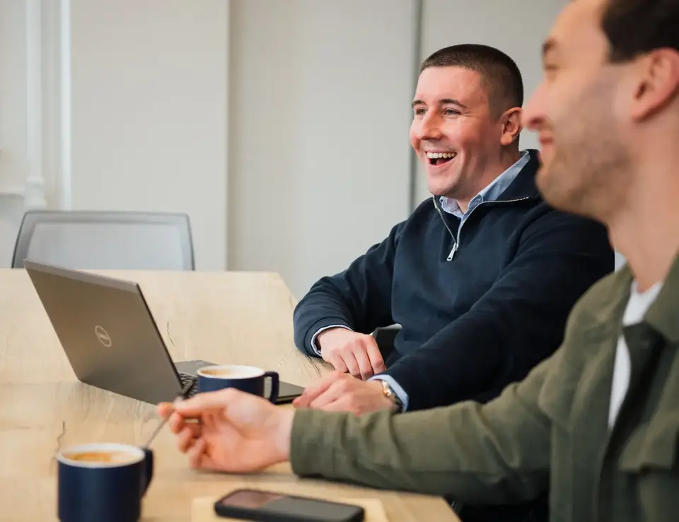 a group of men sitting at a table with coffee and laptop