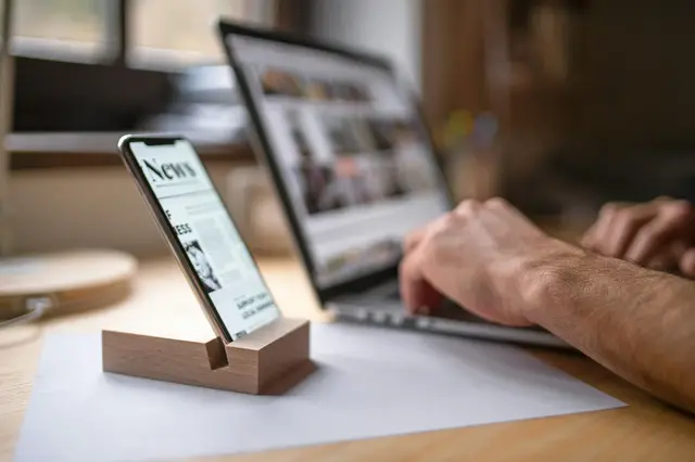 a hand holding a phone in front of a laptop