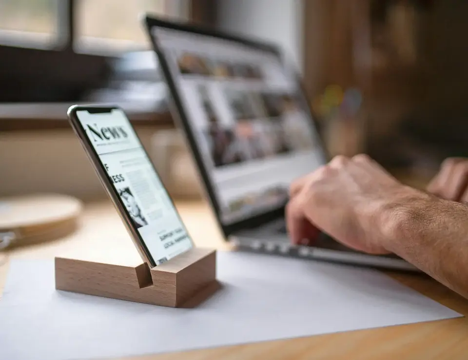 a hand holding a phone in front of a laptop