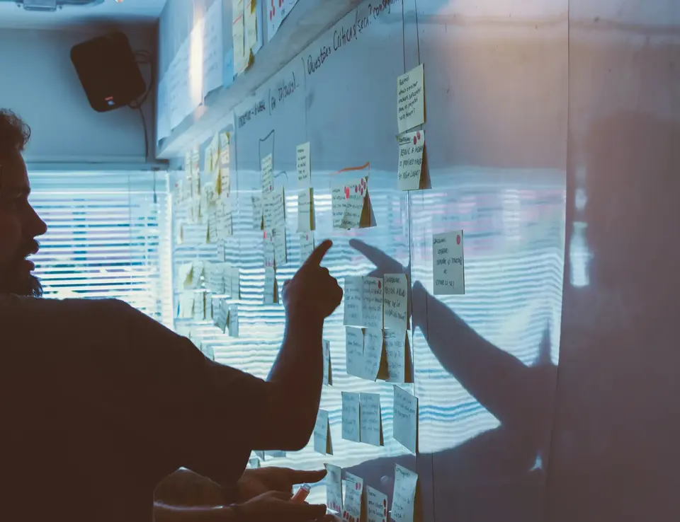 a person pointing at sticky notes on a wall