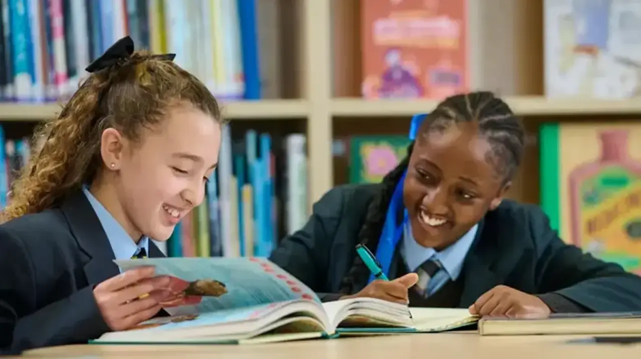 two girls in school uniforms sitting at a table looking at a book