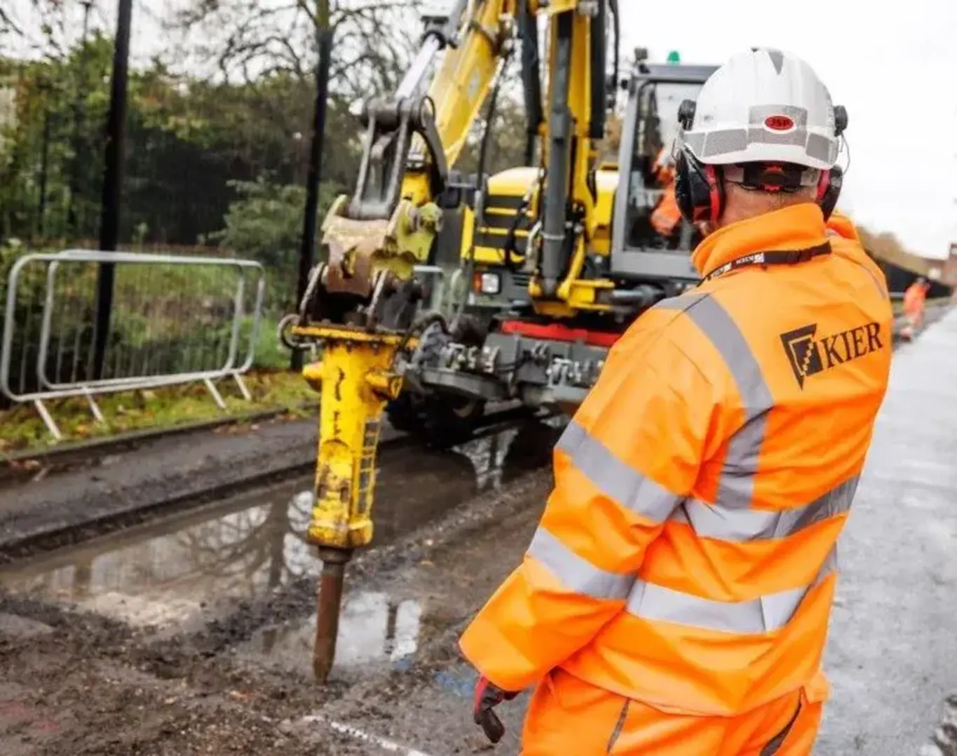 a man in orange jacket and white helmet standing next to a yellow machine