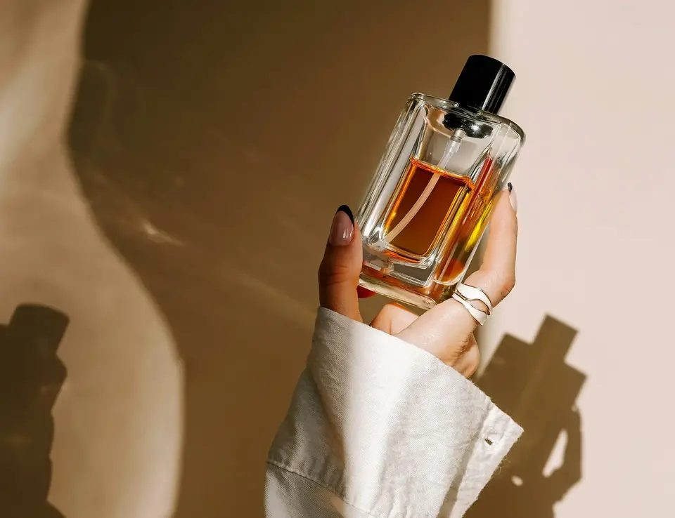 Woman's arm in a white shirt sleeve holding up a glass perfume bottle
