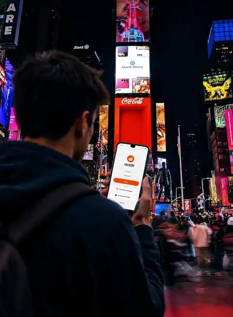 Man holding phone in Times Sqaure, the phonescreen shows the Reddit login page