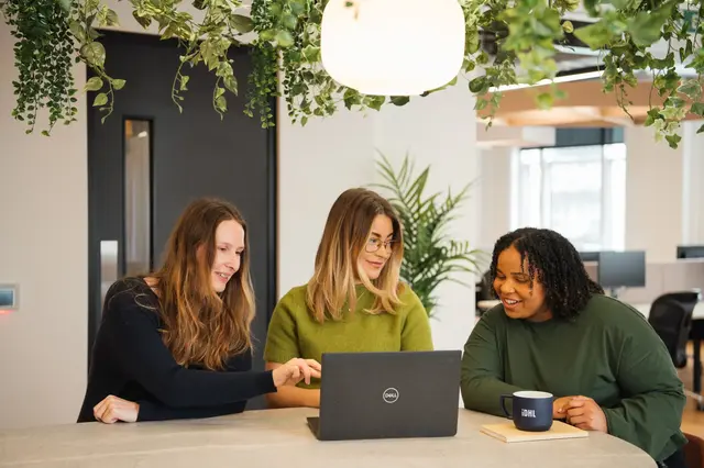 a group of women sitting at a table looking at a laptop